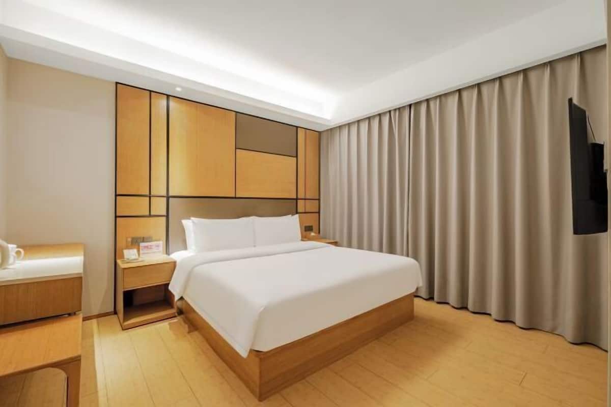 A hotel room with a bed, a desk, a nightstand, a TV, and curtains.