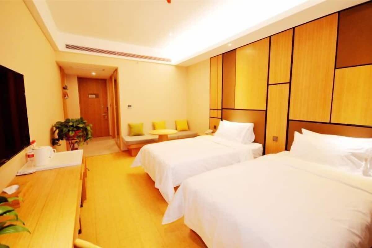 A hotel room with two beds, a desk, a TV, and a seating area with cushions.