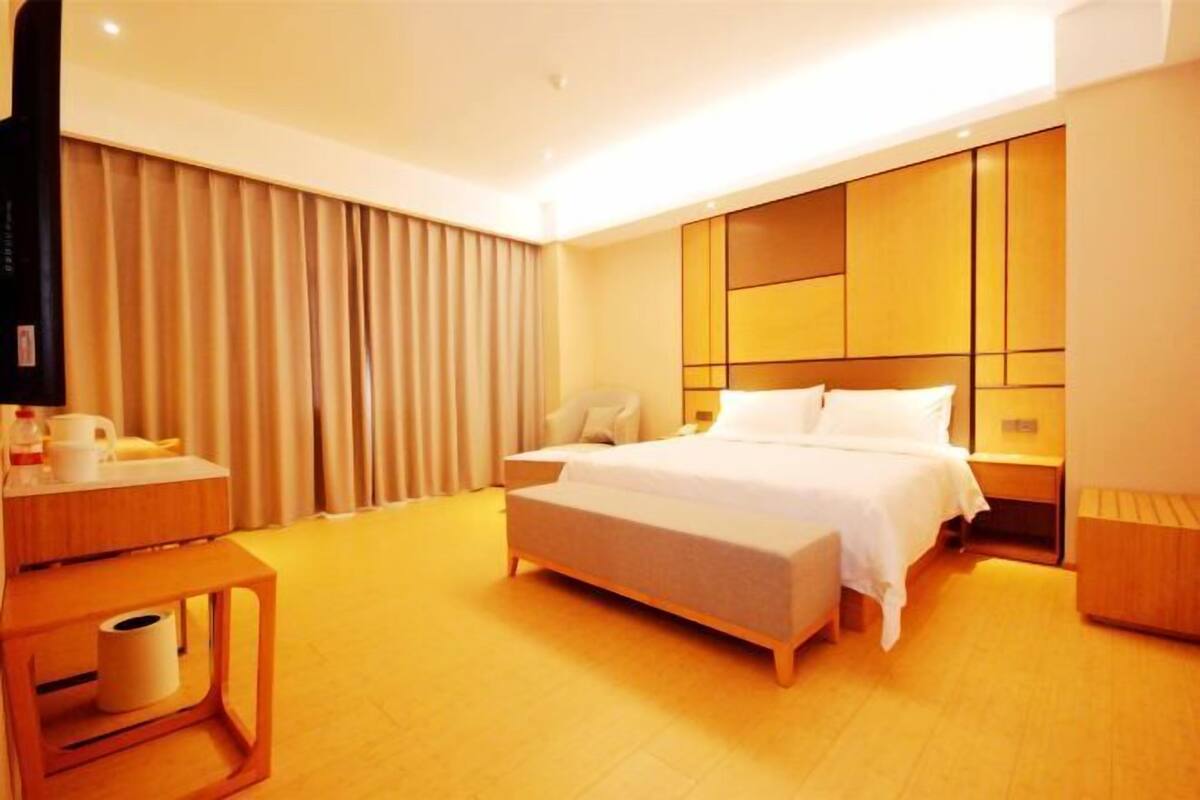 A hotel room with a bed, bedside table, lamp, curtains, and a television.