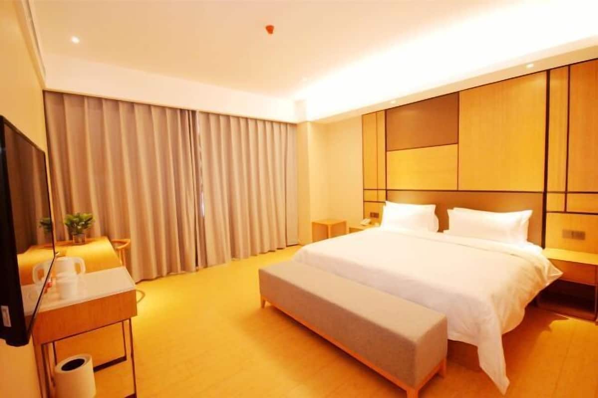 A hotel room with a bed, bedside tables, a desk, a chair, a TV, and curtains.