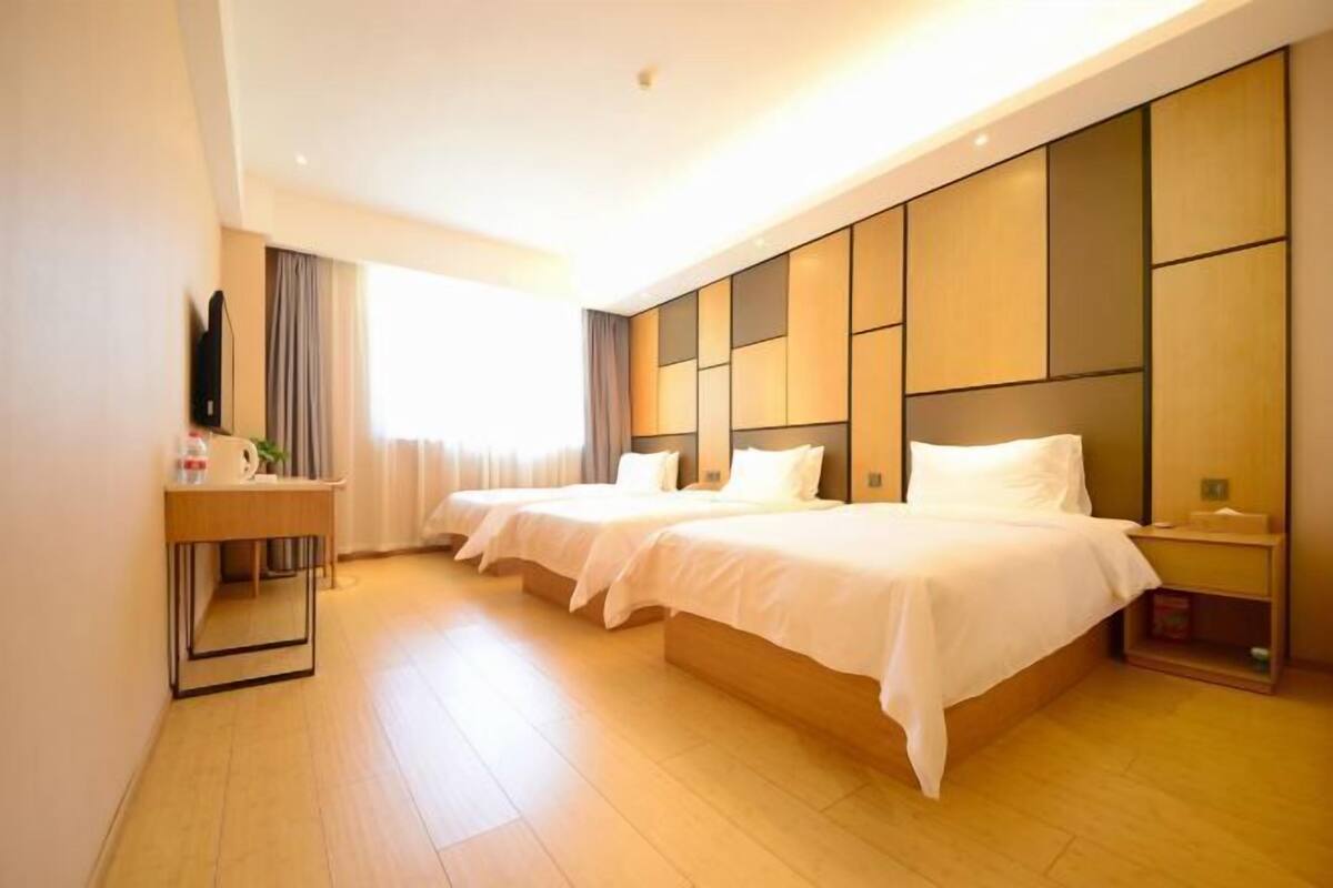 A hotel room with two beds, a bedside table, a TV, and a window with curtains.