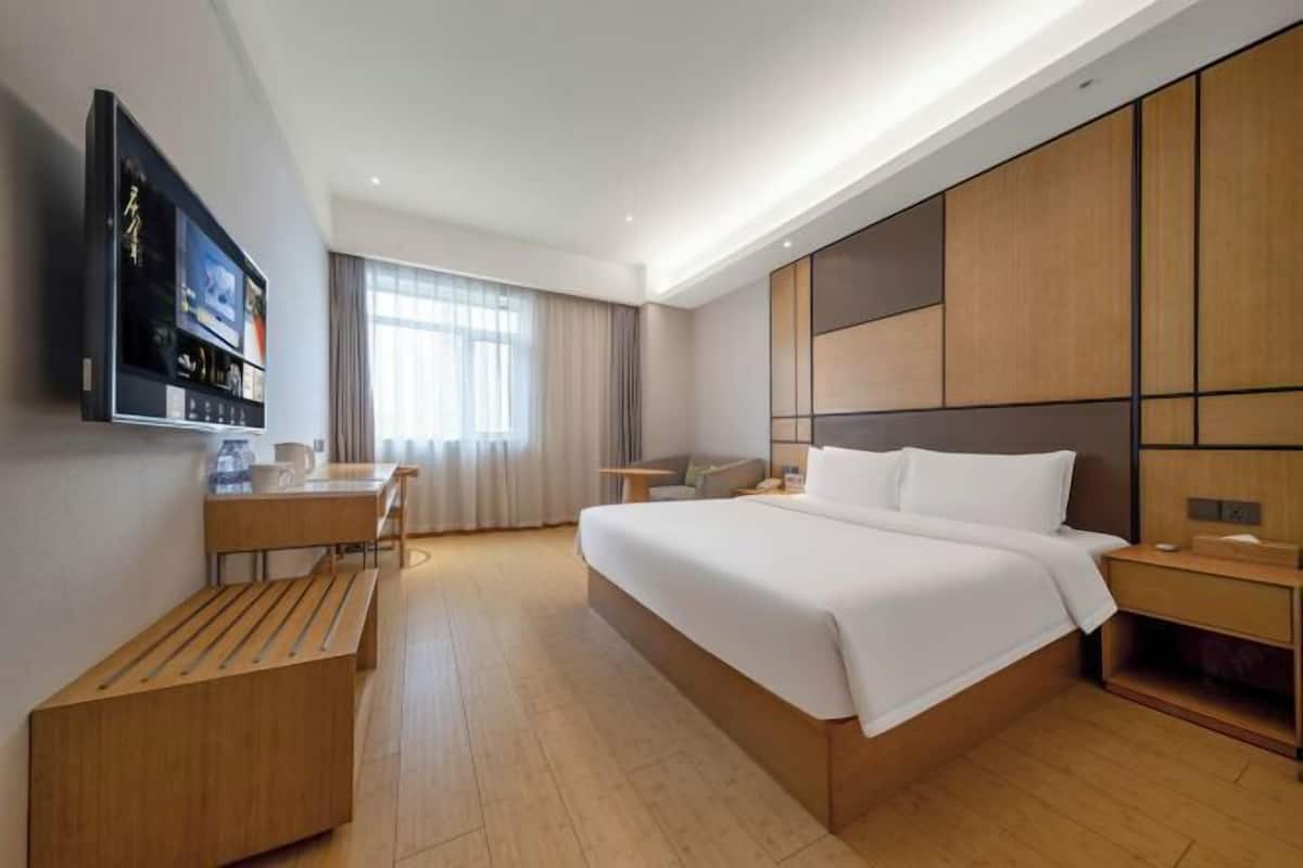 A modern hotel room with a large bed, a desk, a TV, and a view of the outdoors.