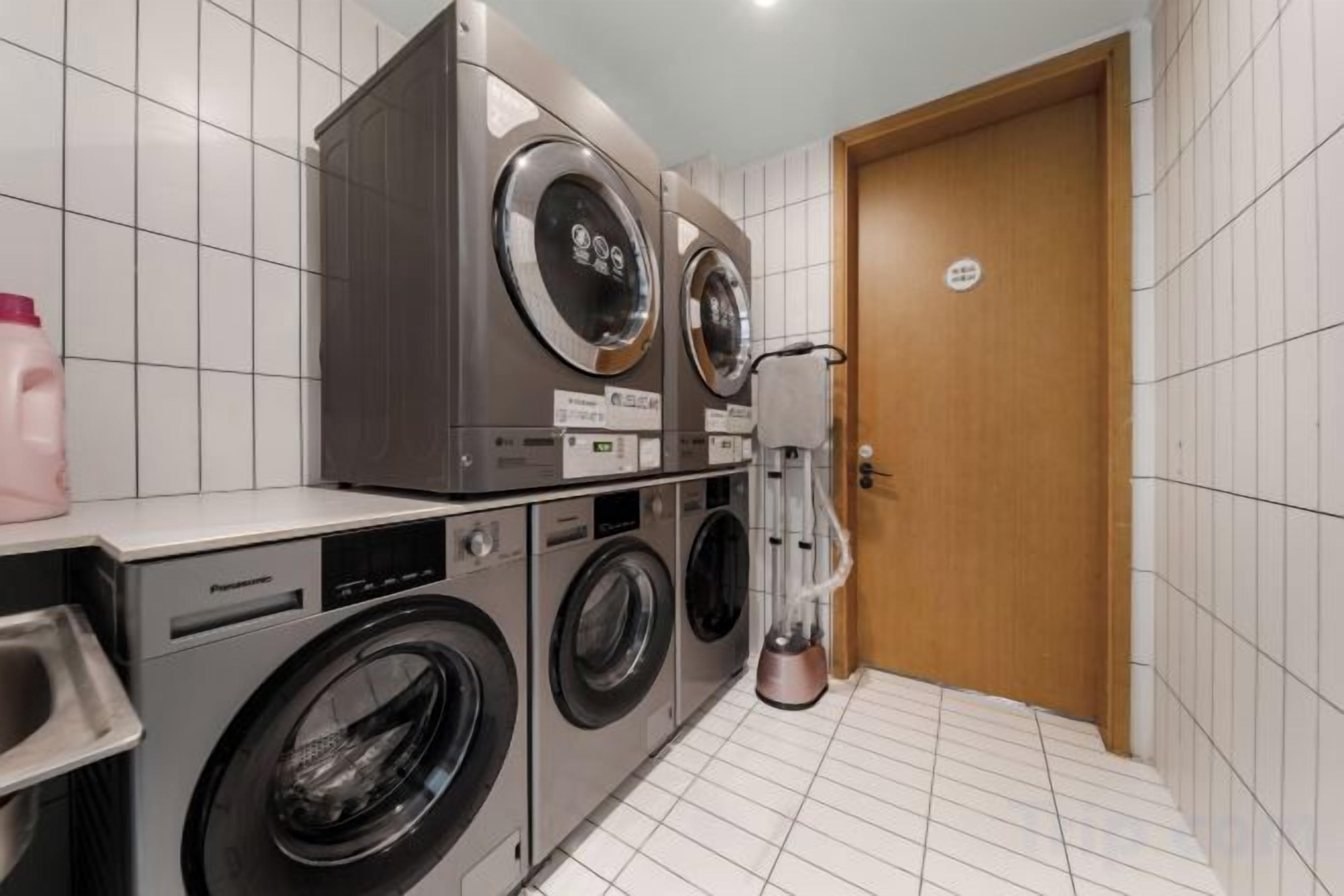 A laundry area with stacked washing machines and a dryer, a sink, and a door with a sign.