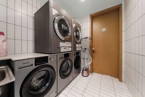 A laundry area with stacked washing machines and a dryer, a sink, and a door with a sign. - Yoke Hotel (Taiyuan)