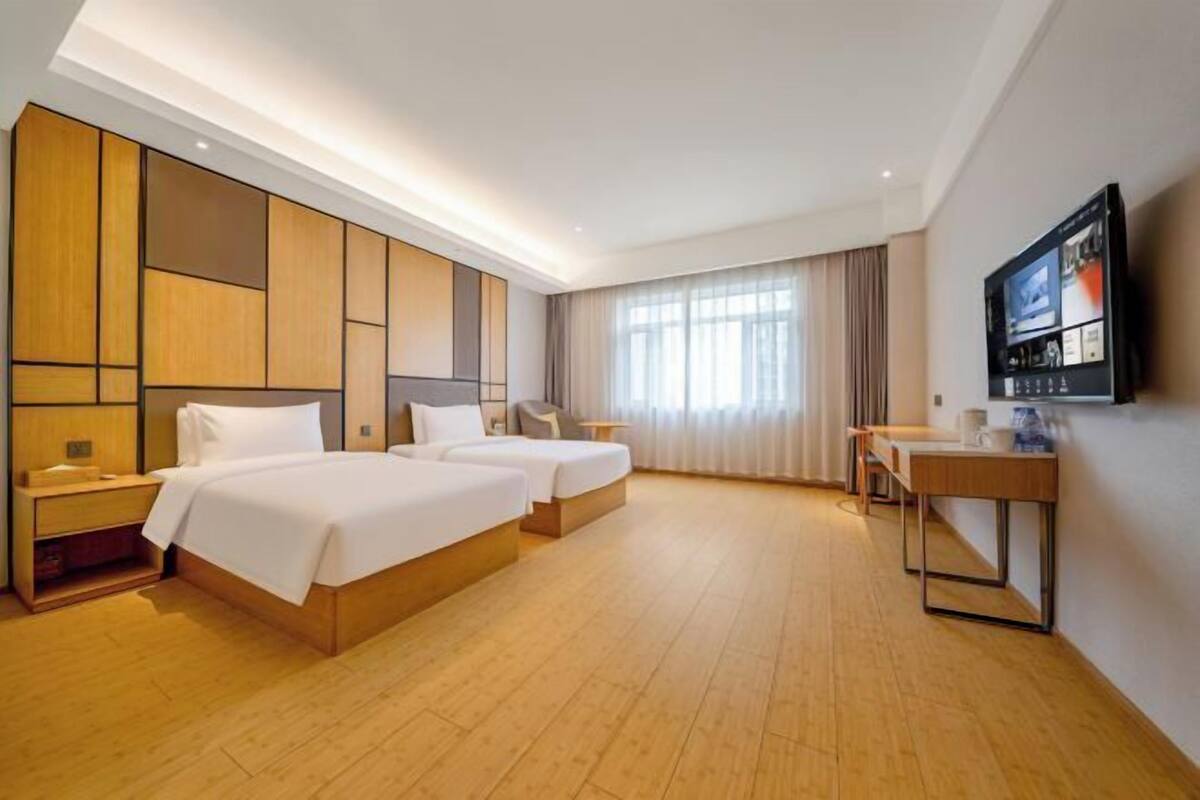 A hotel room with two beds, a desk, a TV, and a large window.