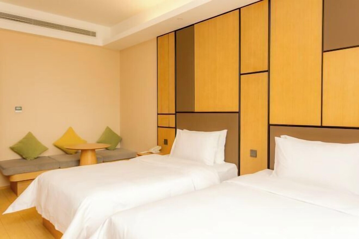 A hotel room with two beds, a small round table, and a sofa with cushions.
