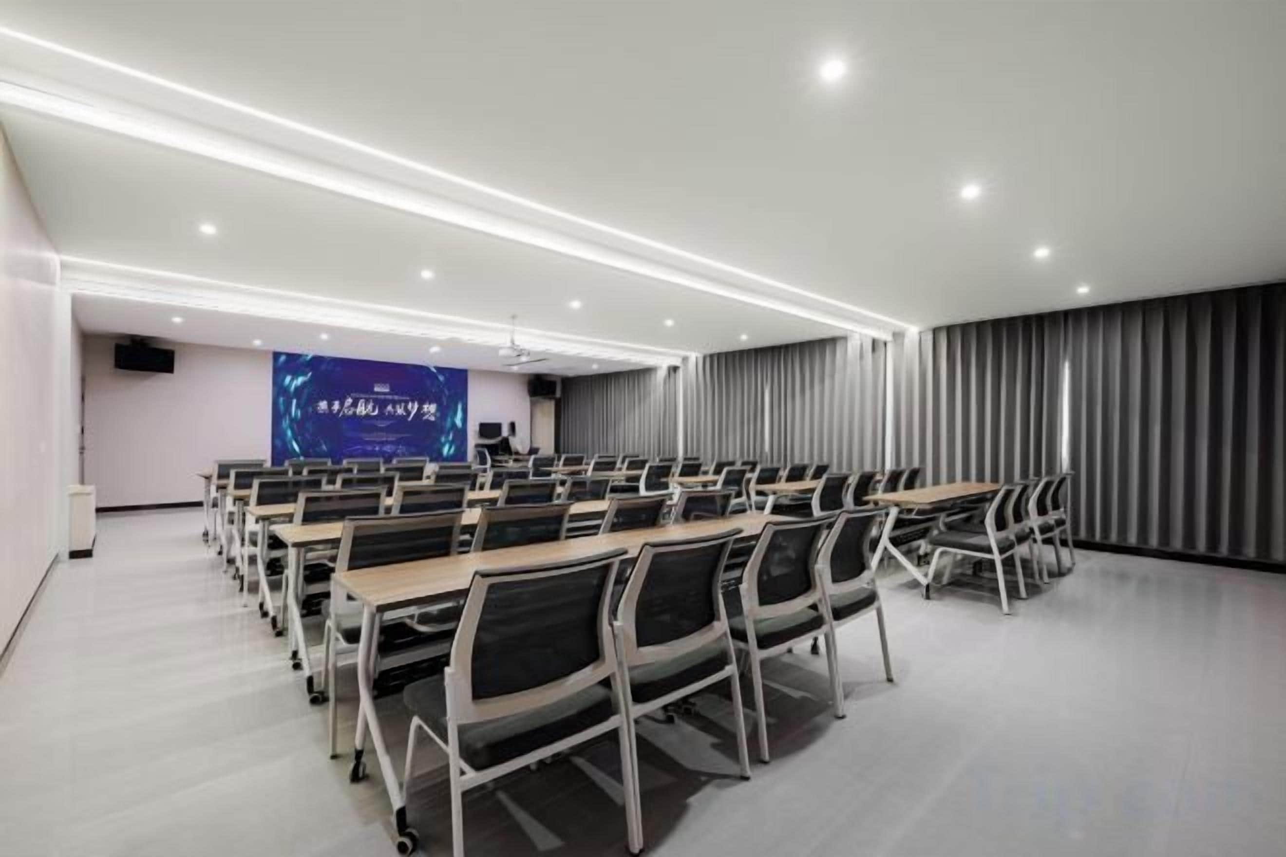 A conference room with rows of tables and chairs, a presentation screen, and a projector.
