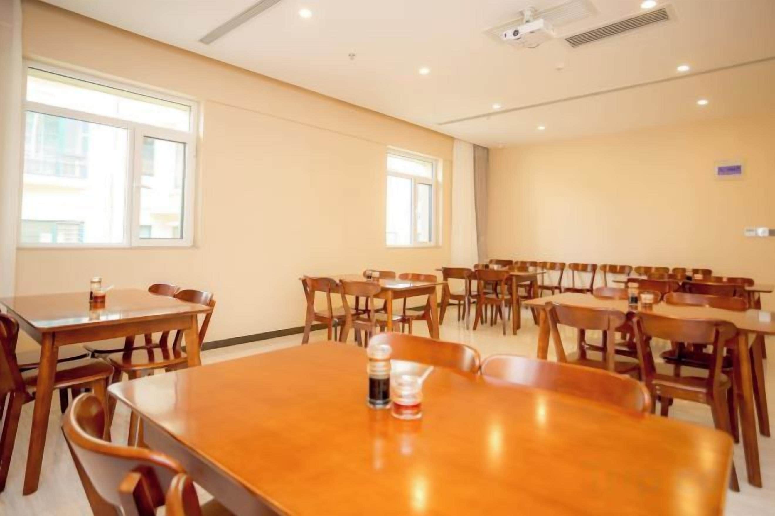Uma sala de conferências com várias mesas e cadeiras, janelas amplas e um projetor no teto.