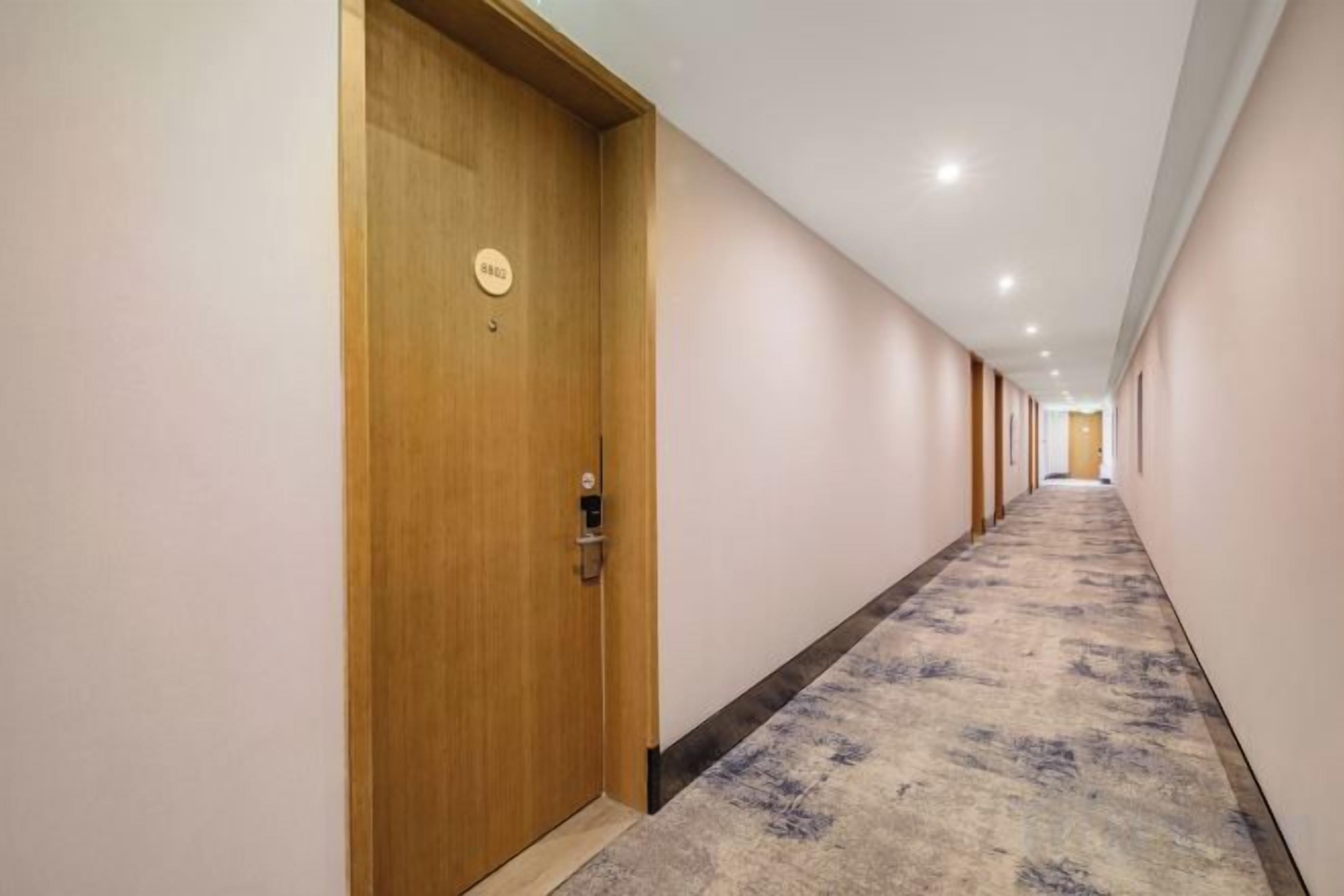 A hotel corridor with a carpeted floor, wooden doors, and a ceiling with recessed lighting.