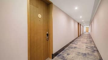 A hotel corridor with a carpeted floor, wooden doors, and a ceiling with recessed lighting.