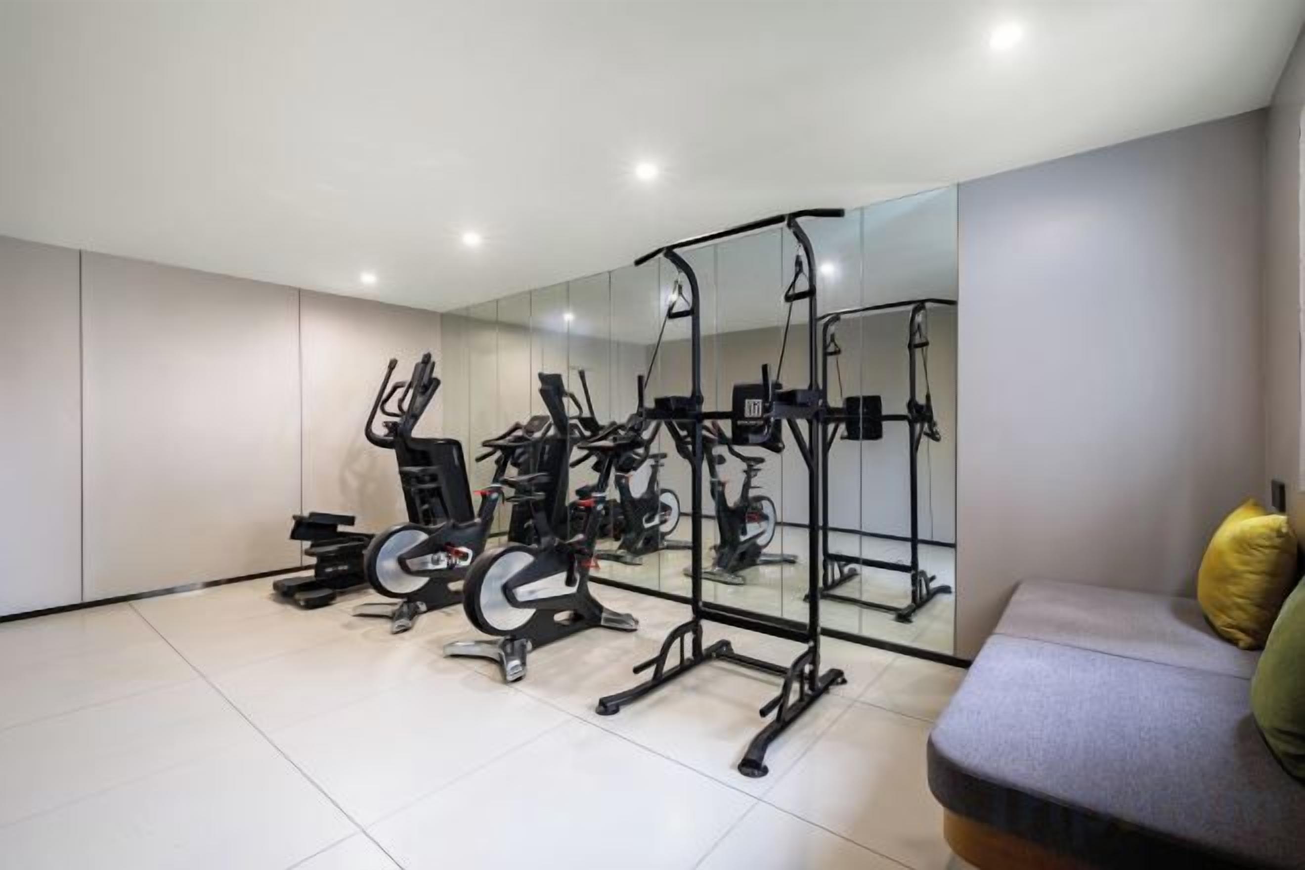 Un gimnasio moderno con equipamiento de ejercicio, un espejo grande y una zona de descanso.