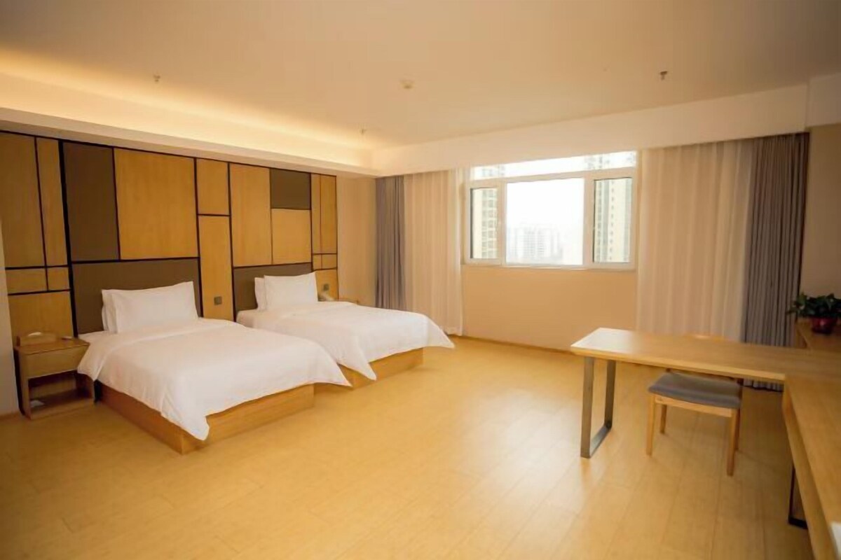 A modern hotel room with two beds, a wooden desk, and a large window.