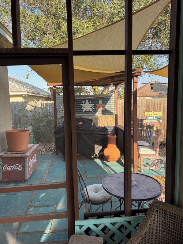 A screened outdoor patio with a table and chairs, a Coca-Cola cooler, and a grill.