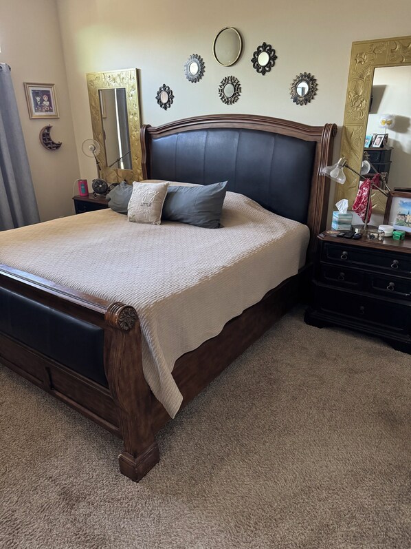 A neatly made bed with a dark headboard, a bedside table with a lamp, and decorative wall mirrors.