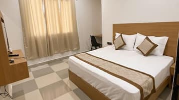 A hotel room with a checkered floor, a bed with a wooden frame, a bedside table, a chair, and an air conditioning unit.