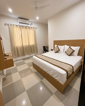 A hotel room with a checkered floor, a bed with a wooden frame, a bedside table, a chair, and an air conditioning unit.