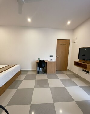 Une pièce comprenant un lit, un bureau, une chaise, un téléviseur et une porte.