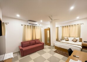 Une chambre d’hôtel avec un lit, un canapé rouge, un bureau avec une chaise et un ventilateur de plafond.