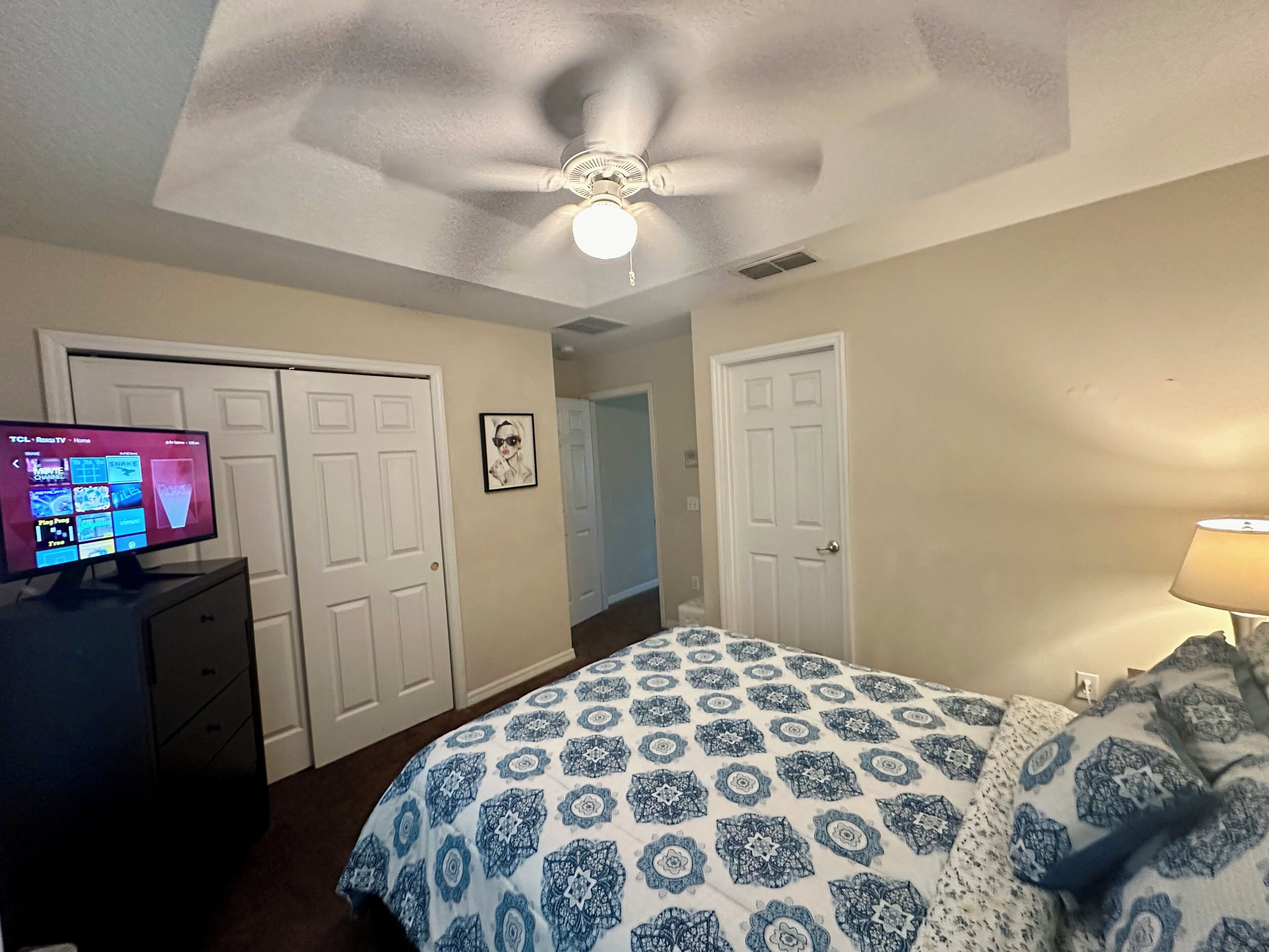 Ein Schlafzimmer mit einem Bett, einem Fernseher auf einer Kommode und einem Deckenventilator.