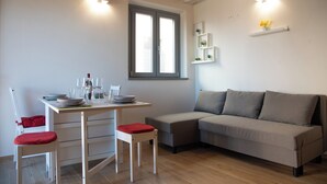 Ein modernes Wohnzimmer mit Essbereich, ausgestattet mit einer Couch, einem Esstisch, Stühlen und einem Fenster mit Jalousien.