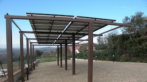 Eine Pergola aus Metall mit Kiesboden, umgeben von einem Zaun und Bäumen.
