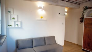 Ein modernes Wohnzimmer mit grauem Sofa, weißen Regalen mit Pflanzen und einem Holzkabinett.