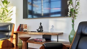 Un saló modern amb butaques de cuir, una taula baixa de fusta, una estanteria i un gran televisor de pantalla plana fixat a la paret.