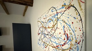 Ein Zimmer mit einem großen, abstrakten Gemälde an der Wand, einem dunkelblauen Schrank und freiliegenden Holzbalken.