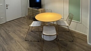 Ein Essbereich mit einem runden Tisch, vier Stühlen, einem Fernseher und einer Pendelleuchte.
