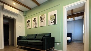 Ein geräumiges Wohnzimmer mit einem grünen Sofa, Holzboden und einer Decke mit freiliegenden Balken.