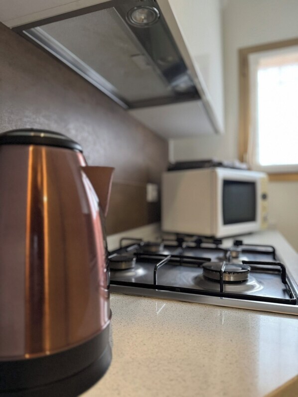 Una cocina con estufa a gas, microondas y hervidor de acero inoxidable.