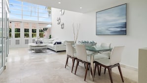 Un interior moderno con una mesa de comedor de vidrio, muebles blancos y un cuadro abstracto de gran tamaño.