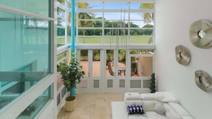 Un interior moderno con un muro de cristal, un sofá blanco y vistas a un patio con mobiliario exterior.