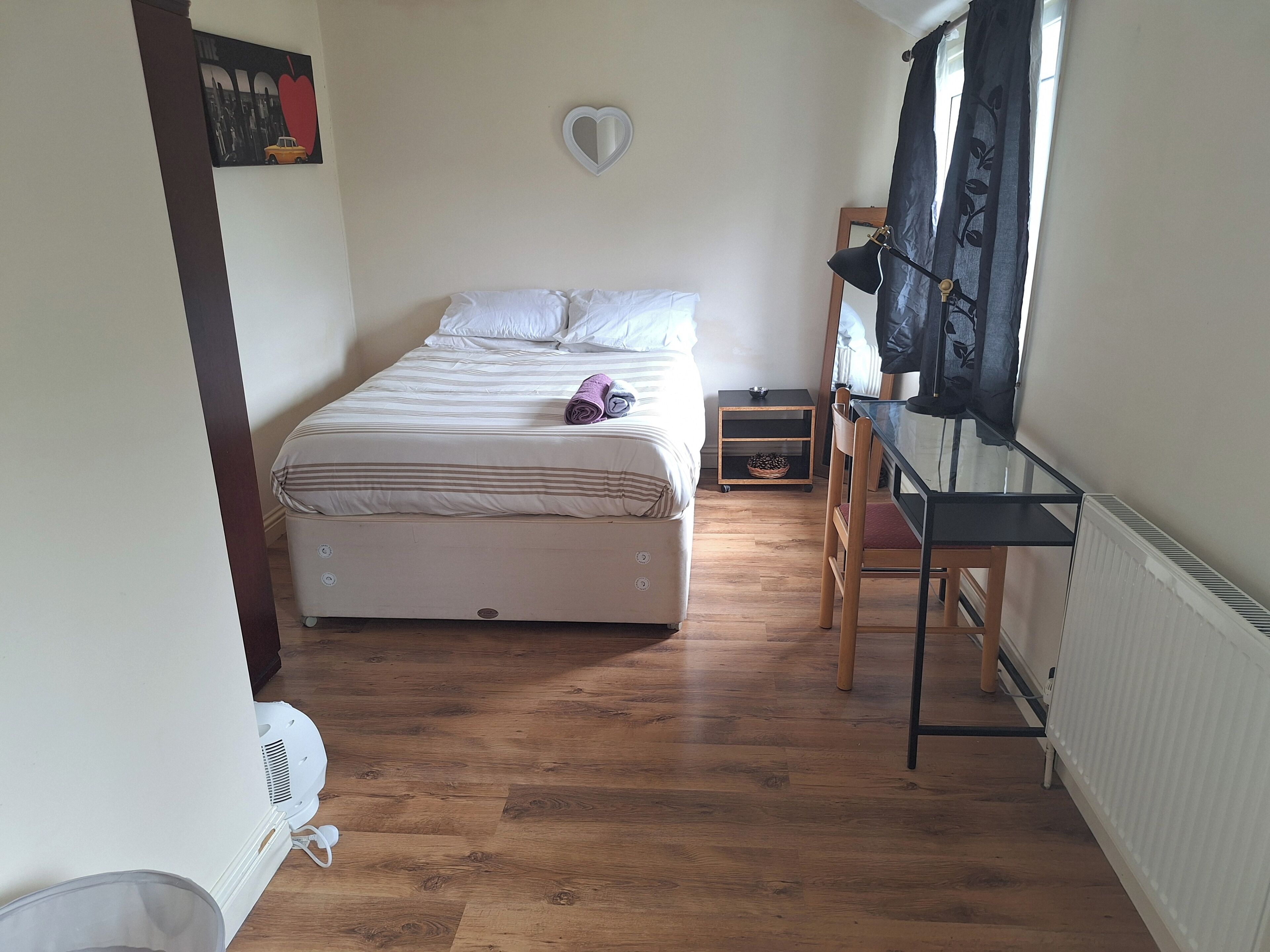 Un dormitorio con cama, una silla, un radiador y una ventana con cortinas.