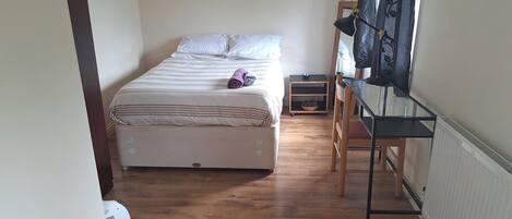 Un dormitorio con cama, una silla, un radiador y una ventana con cortinas.