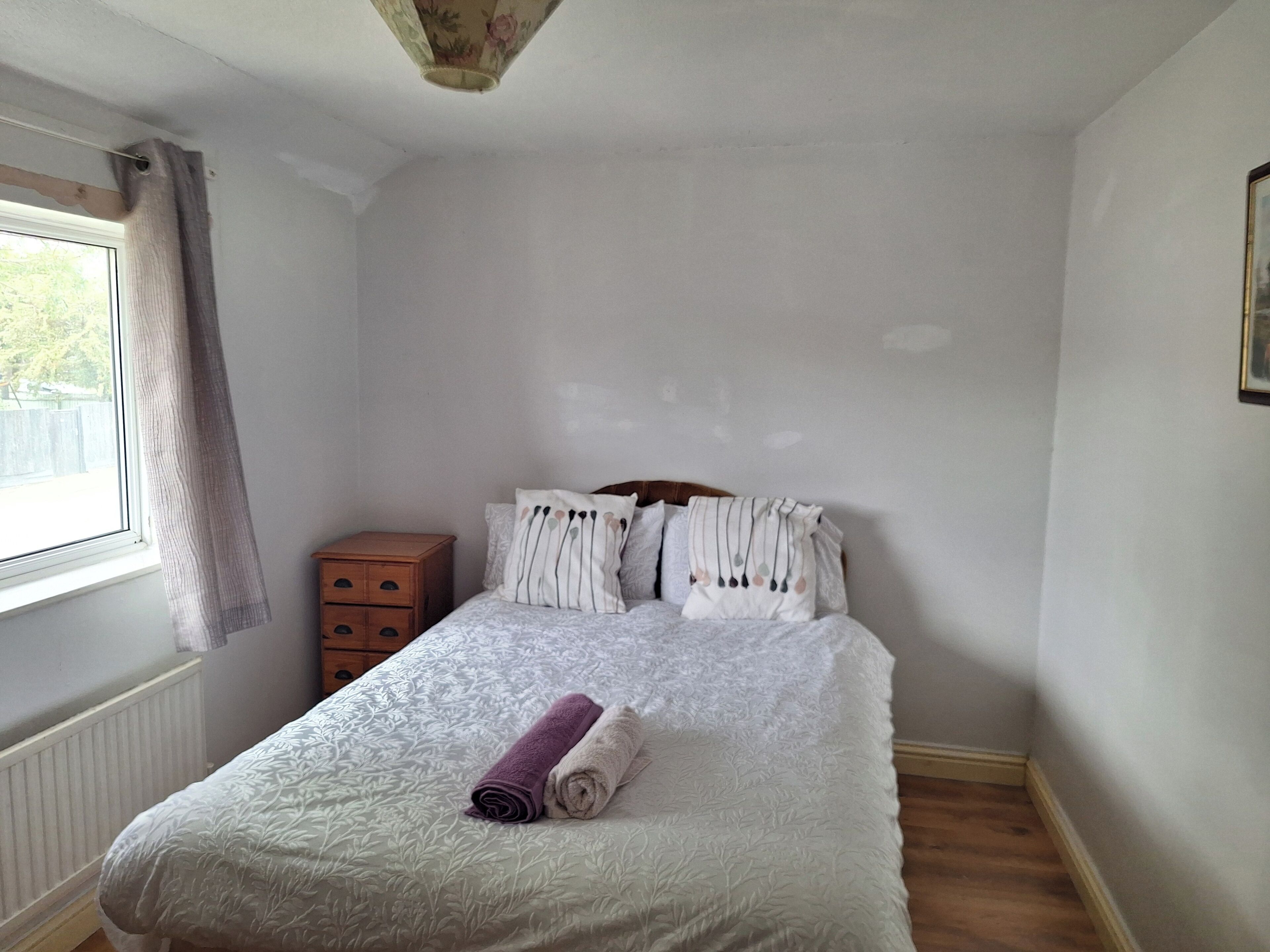 Un dormitorio con cama, mesita de noche, ventana con cortinas y radiador.