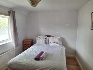 Un dormitorio con cama, mesita de noche, ventana con cortinas y radiador.