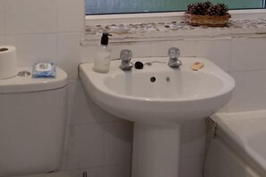 Un baño con lavamanos blanco, inodoro y ventana con vista a piñas.