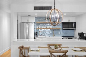 A modern kitchen with white cabinetry, a stainless steel refrigerator, a built-in oven, and a coffee maker.
