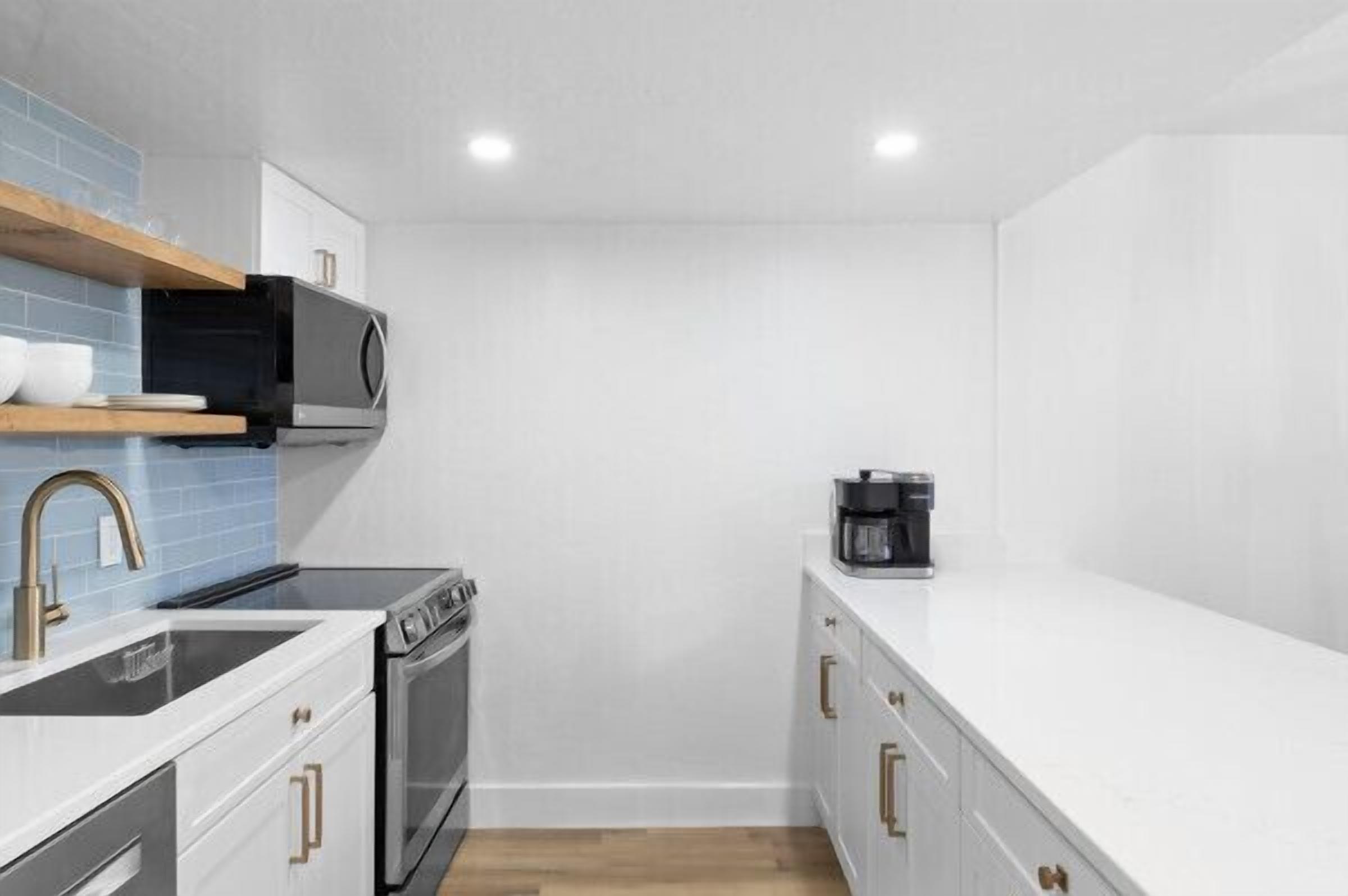 A compact kitchen with white cabinets, a black microwave, a coffee maker, and a stainless steel sink.