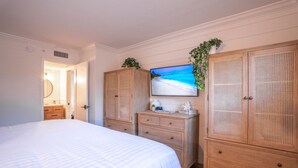 A bedroom with a large bed, wooden wardrobe, and a television on the wall.