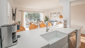 A modern kitchen with a built-in sink, a coffee maker, wicker chairs, and a view of the outdoors.