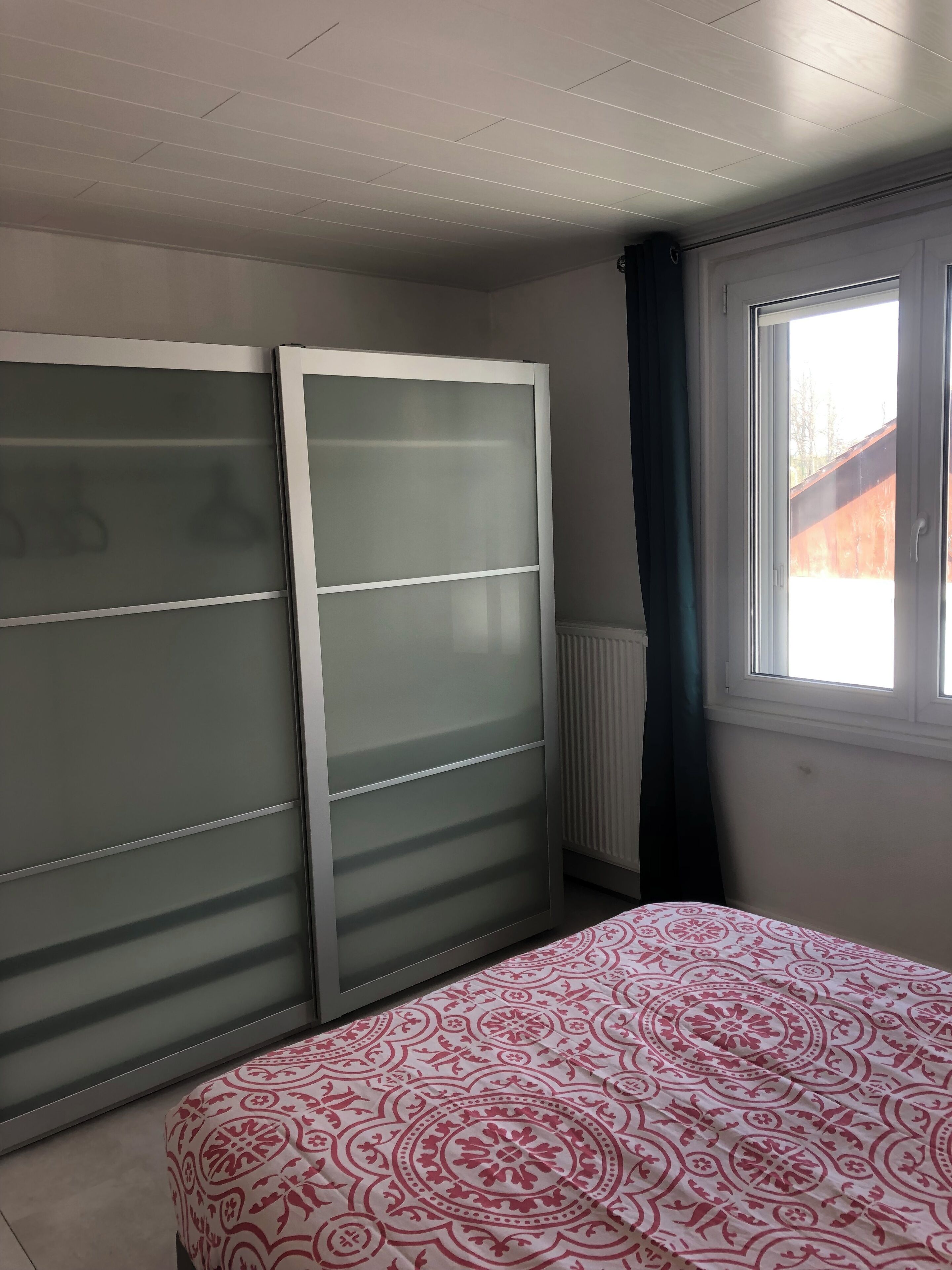 A bedroom with a bed, a wardrobe, a radiator, and a window with curtains.