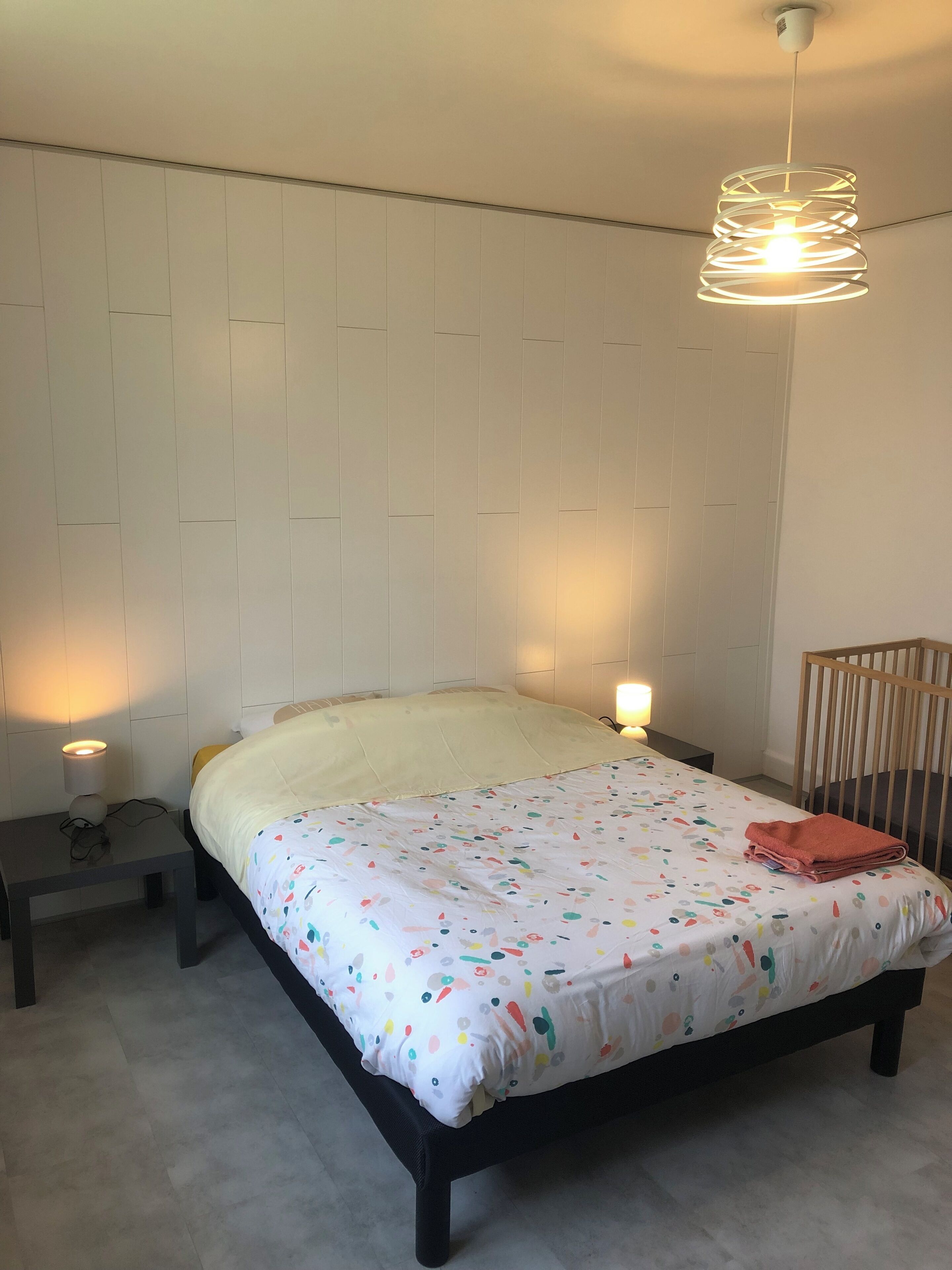 Una camera da letto con un letto, lampade da comodino, una culla e un lampadario.