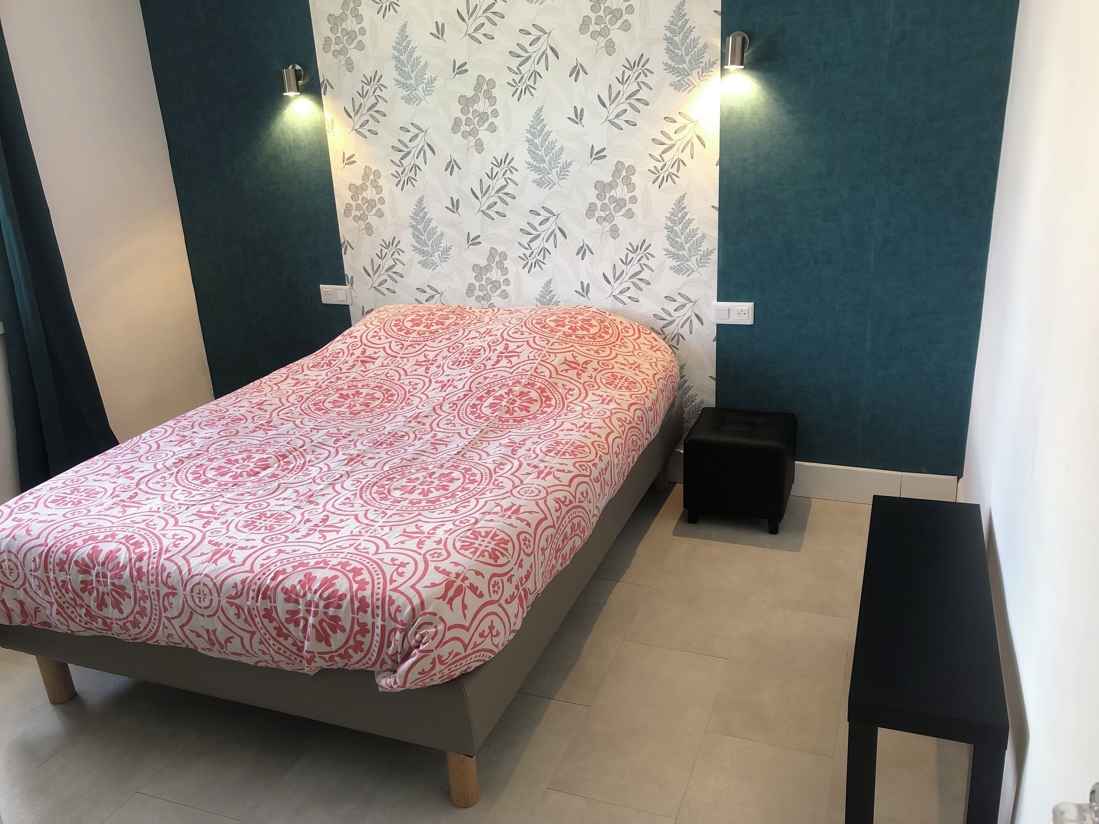 A bedroom with a bed, two wall-mounted lights, a small black nightstand, and a patterned wallpaper.