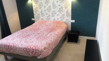 A bedroom with a bed, two wall-mounted lights, a small black nightstand, and a patterned wallpaper.