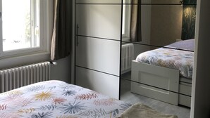 Un dormitorio con cama, armario, radiador y ventana con cortinas.