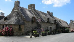 A row of stone buildings with thatched roofs, likely part of a historic village. - Cottage in the heart of the village of Kerascoët. (NEVEZ)