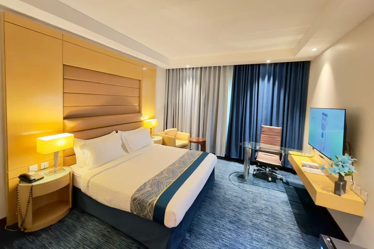 Une chambre d’hôtel avec un grand lit, des lampes de chevet, un bureau avec un ordinateur, une chaise et un téléviseur.