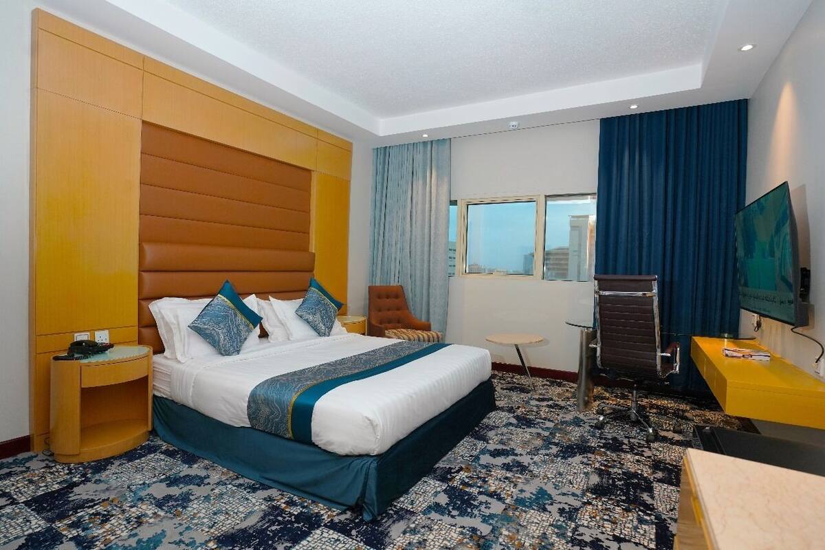 Une chambre d’hôtel avec un grand lit, un bureau, une chaise, une télévision et une fenêtre avec des rideaux.